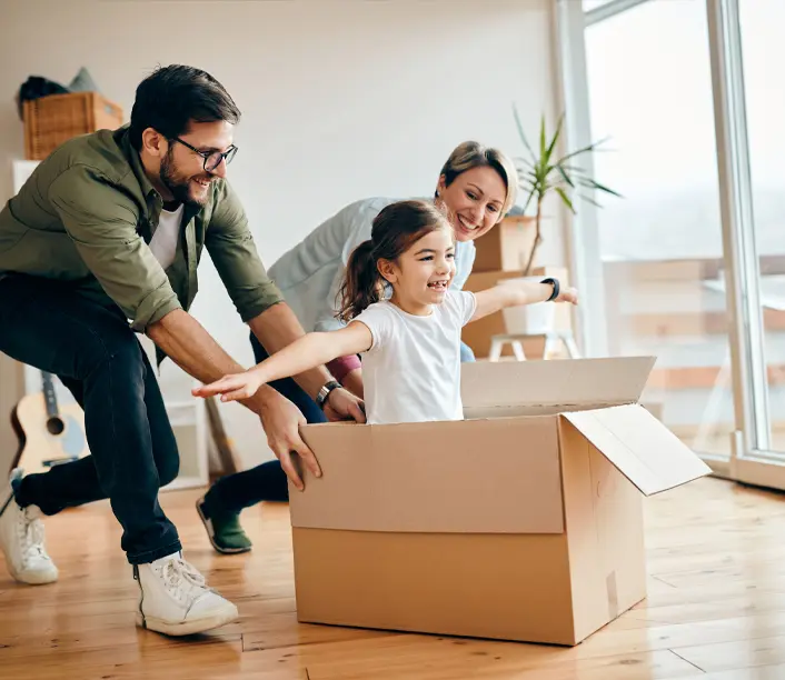 Familie mit Kind packt in einem hellen Raum einen Umzugskarton aus