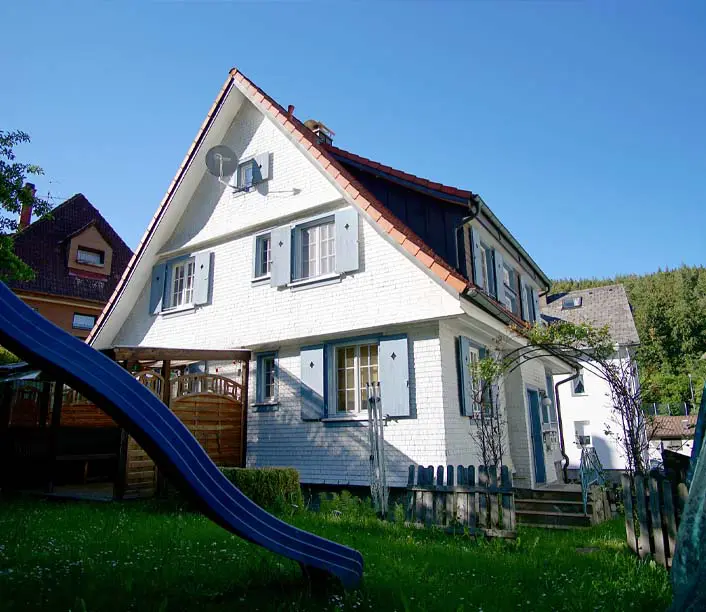 Weißes Wohnhaus mit Fensterläden und Kinderrutsche im Garten