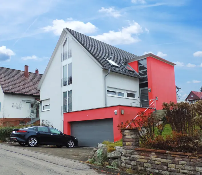 Wohnhaus mit weißer Fassade, rotem Garagenanbau und Auffahrt