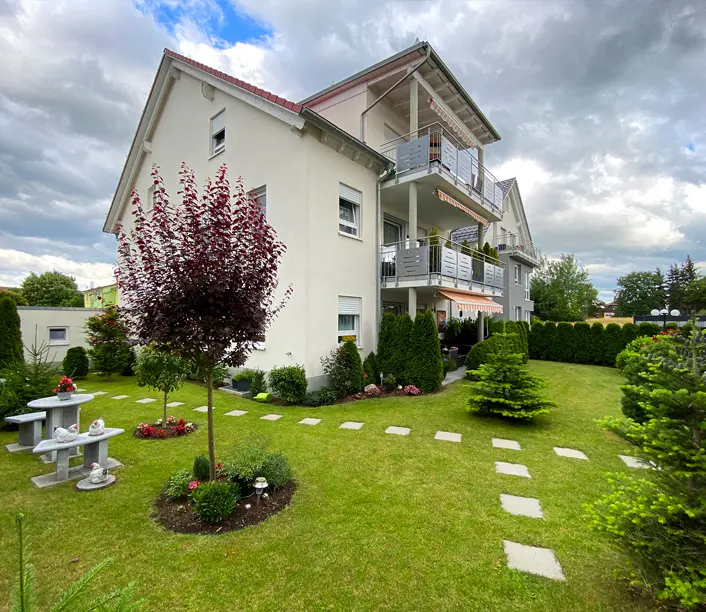 Weißes Mehrfamilienhaus mit Balkonen, Zierbaum und gepflegter Rasenfläche